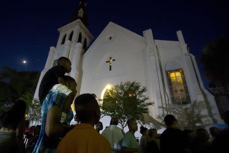 A father carries his son on his back as they listen to gospel music being sung during a vigil outside Emanuel African Methodist Episcopal Church in Charleston, June 20, 2015. REUTERS/Carlo Allegri