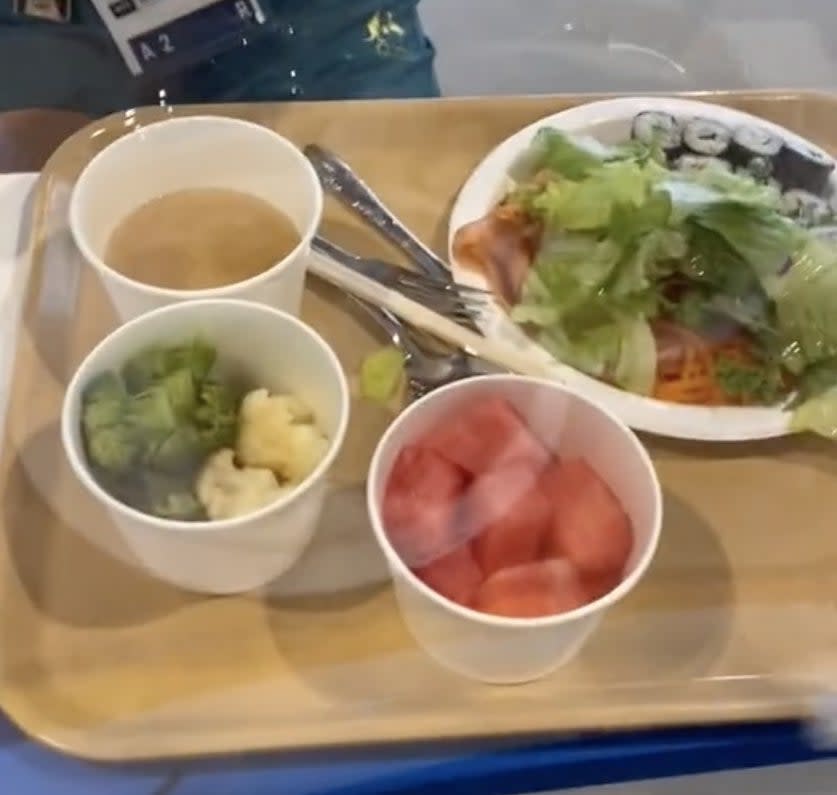 A tray filled with food including a salad, watermelon and broccoli