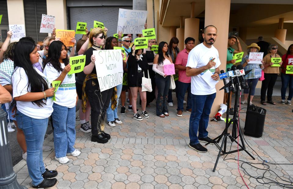 Rene Gomez with Hope Community Center, speaks to the media, with protestors behind him, outside the Sarasota County Commission chambers on Friday. The commission was holding a workshop about how much illegal immigration is costing the county.