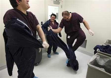 Robert Morris (L-R), Laura Turner and Derek Grice joke as they get out of their sterilized suits after demonstrating how DCVax-L is manufactured in a Northwest Biotherapeutics laboratory in Memphis, Tennessee, February 21, 2014. REUTERS/Mike Brown