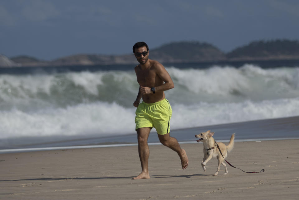 A man runs with his dog on the Copacabana beach during the new coronavirus pandemic in Rio de Janeiro, Brazil, Thursday, July 2, 2020. Rio de Janeiro authorities have begun to ease the city's lockdown amid the growing COVID-19 pandemic. (AP Photo/Silvia Izquierdo)