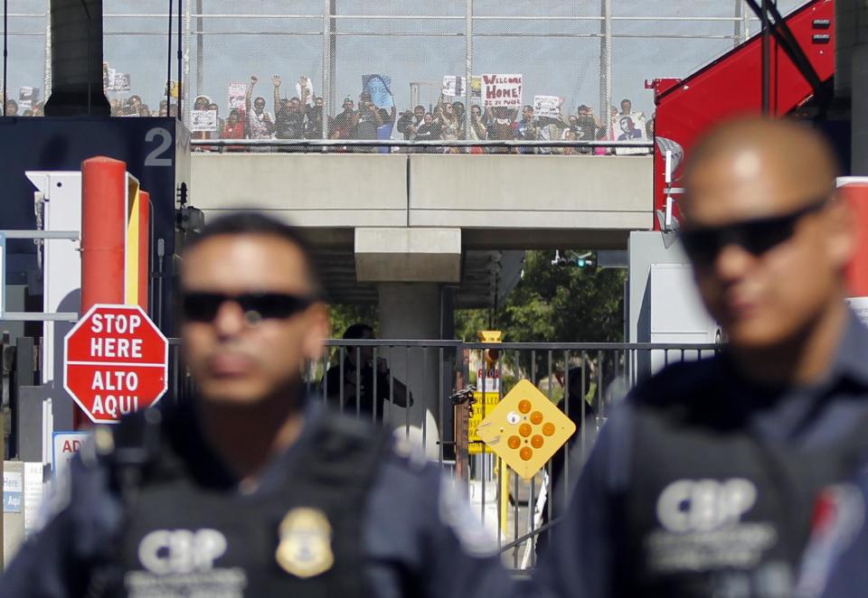 Demonstrators supporting the group Border Dreamers and other advocates for an open border policy hold signs while lining a walking bridge inside United States behind Customs and Border Protection officers who are blocking the vehicle entrance to the United States Monday, March 10, 2014, in Tijuana, Mexico. (AP Photo/Lenny Ignelzi )