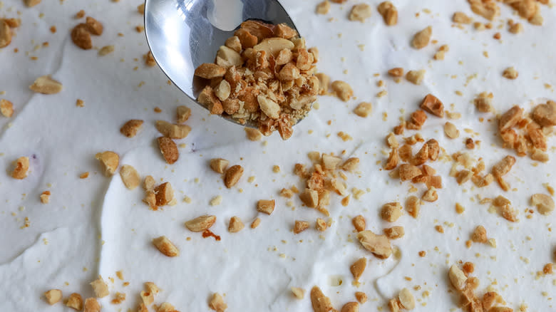 peanuts being sprinkled on whipped topping with a spoon