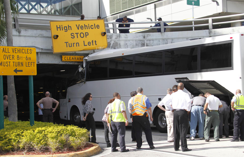 Workers and law enforcement officers prepare to remove a bus after it hit a concrete overpass at Miami International Airport in Miami on Saturday, Dec. 1, 2012. The vehicle was too tall for the 8-foot-6-inch entrance to the arrivals area, and buses are supposed to go through the departures area which has a higher ceiling, according to an airport spokesperson. (AP Photo/Wilfredo Lee)