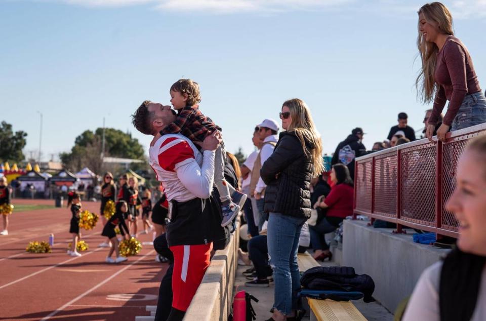 Wide receiver Corey Galindo, left, with the statewide fire service Fire Dogs, receives his 2-year-old son Cruz from his wife, Candice Galindo, right, after scoring against the Sacramento region law enforcement Hogs in the second quarter at the 49th Pig Bowl on Saturday, Jan. 28, 2023, at Hughes Stadium at Sacramento City College. Galindo, who played football at UC Davis and workers as a firefighter in Riverside, was named MVP after the Fire Dogs beat the Hogs, 12-5.