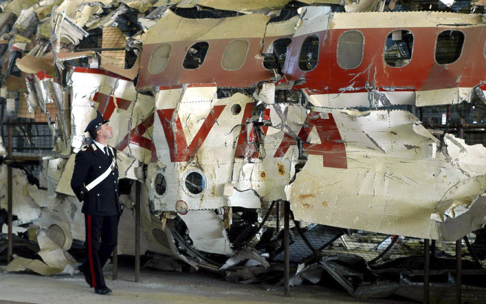 FILE - An Italian Carabinieri police officer patrols a hangar, in Pratica di Mare, near Rome, Monday Dec. 15, 2003, the reconstructed wreckage of the Itavia DC-9 passenger jetliner which crashed near the tiny Mediterranean island of Ustica in June 27, 1980. A former Italian premier is contending that a French air force missile brought down a passenger jet over the Mediterranean Sea in 1980 and is appealing to France's president to respond. The crash of the Italian domestic airliner killed all 81 persons aboard. What caused the crash is an enduring mystery. (AP Photo/Emiliano Grillotti, File)