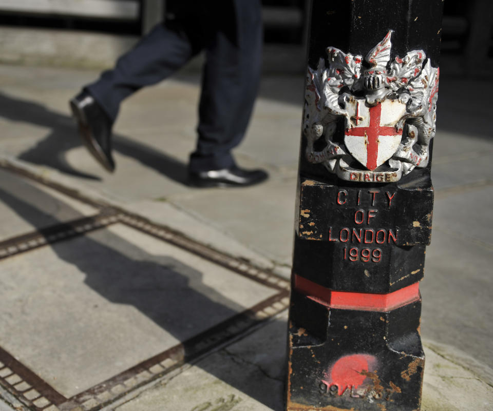 A worker walks past a bollard bearing the coat of arms of the City of London Corporation in London's Square Mile.