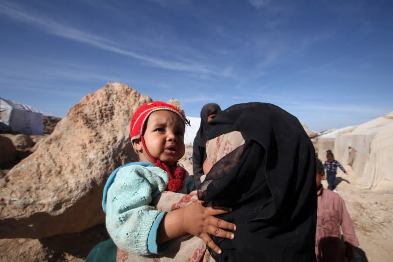 Girl carries her brother in the sun on a cold winter day at a camp for internally displaced people in Khamir of the northwestern province of Amran