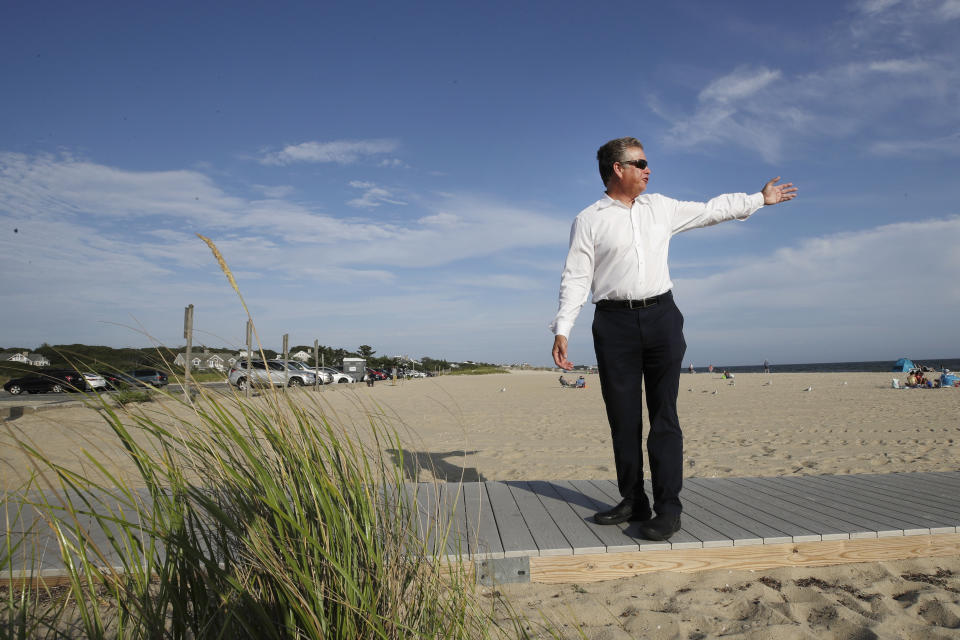 In this Aug. 21, 2019 photo, Andrew Gottlieb, executive director of the Association to Preserve Cape Cod, indicates where the proposed Vineyard Winds' buried energy cables would stretch from offshore wind turbines, through the ocean, under the sand and parking lot at Covell Beach in Centerville, Mass. to a landing point onshore. The cables would then extend to a grid connection point inland. But as Trump has made clear how much he hates wind turbines, all the offshore wind projects, including the nation's first utility-scale offshore wind project, an 84 turbine, $2.8 billion wind farm slated to rise 15 miles off Martha's Vineyard, have stalled. (AP Photo/Elise Amendola)