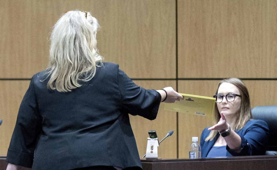 Sherry Culves, an attorney representing the Cobb County School District, hands teacher Katie Rinderle the book "My Shadow is Purple" during a hearing at the Cobb County Board of Education in Marietta, Ga, Thursday, Aug. 10, 2023. Rinderle is facing termination after reading "My Shadow is Purple," a book about gender identity, to fifth graders. (Arvin Temkar/Atlanta Journal-Constitution via AP)