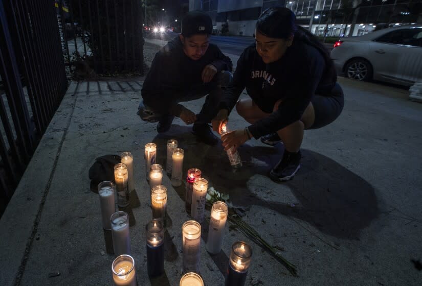 LOS ANGELES, CA - December 19 2021: A couple light candles at a makeshift memorial on Martin Luther King Jr. Blvd. on Martin Luther King Jr. Blvd. in honor of slain rapper Drakeo the Ruler on Sunday, Dec. 19, 2021 in Los Angeles, CA. (Brian van der Brug / Los Angeles Times