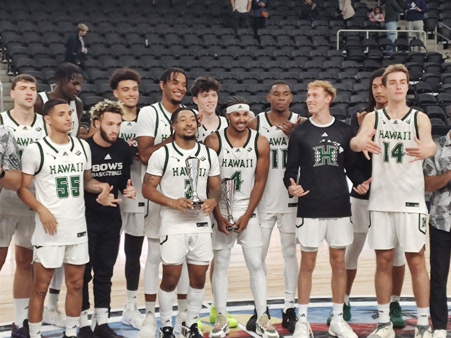 The University of Hawaii basketball team celebrates while holding the trophy as the inaugural Acrisure Invitational champions Saturday at Acrisure Arena, after defeating San Diego 77-66 in the title game.