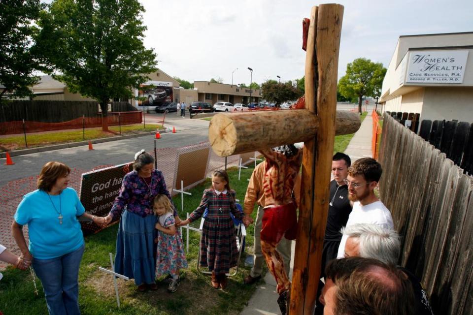 people hold hands in a circle near a cross