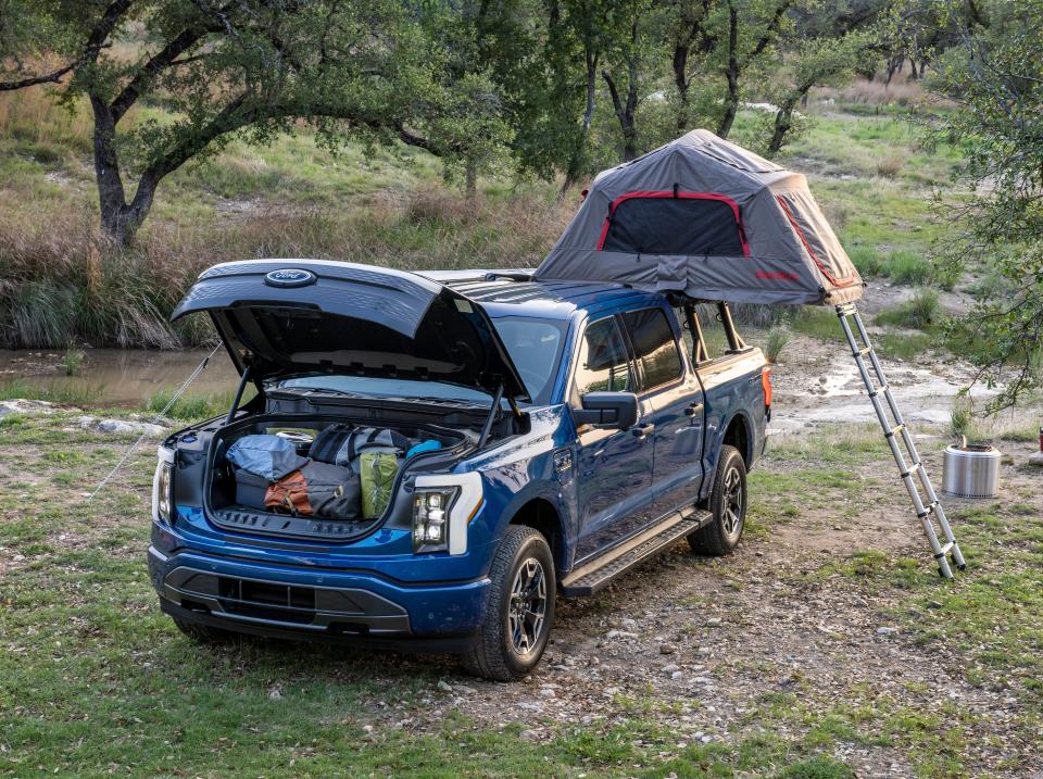 A blue truck filled with camping gear and a tent in the middle of a wooded area.