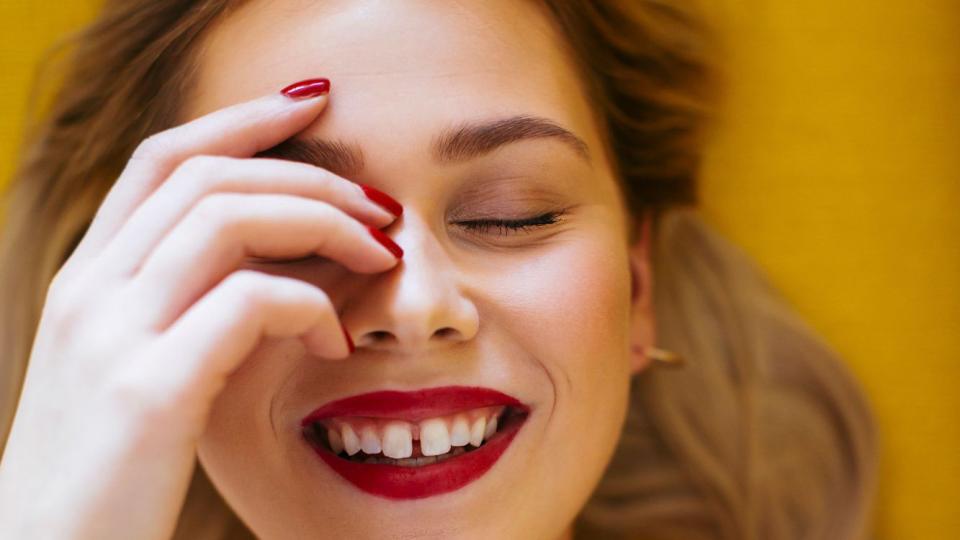 Person with a gap-toothed smile wearing red lipstick and nails.