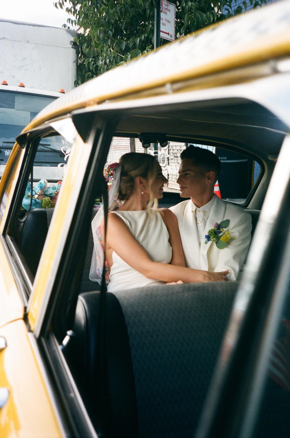 Two brides look at each other in the back of a taxi.