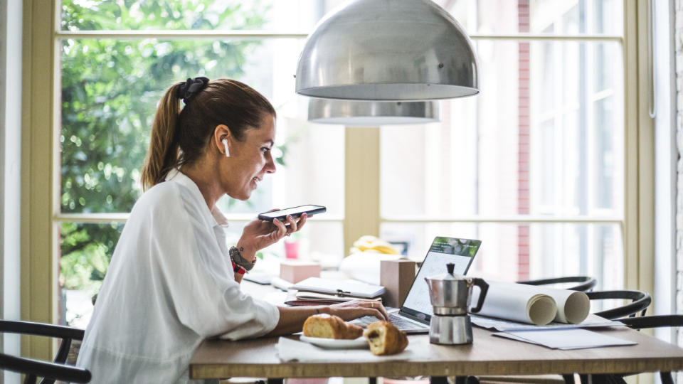 Woman on phone working from kitchen bench.