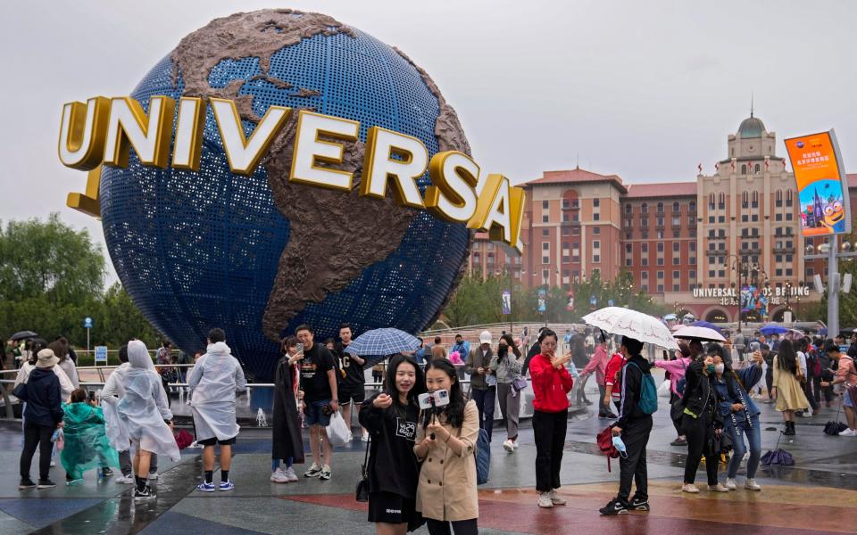 People take selfies with an icon near the entrance to Universal Studios Beijing in Beijing, Monday, Sept. 20, 2021. Thousands of people brave the rain visit to the newest location of the global brand of theme parks which officially opens on Monday. (AP Photo/Andy Wong) - AP Photo/Andy Wong