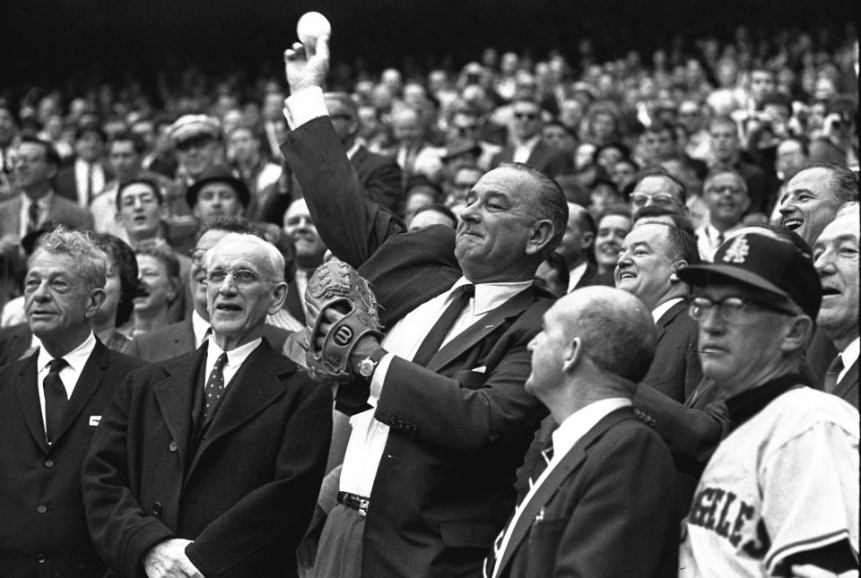 FILE - In this April 13, 1964, file photo, President Lyndon Johnson throws out the first pitch to open the American League baseball season in Washington. The first pitch ceremony preceded the opening game between the Los Angeles Angels and the Washington Senators. At left is House Speaker John McCormack of Massachusetts. (AP Photo/File)