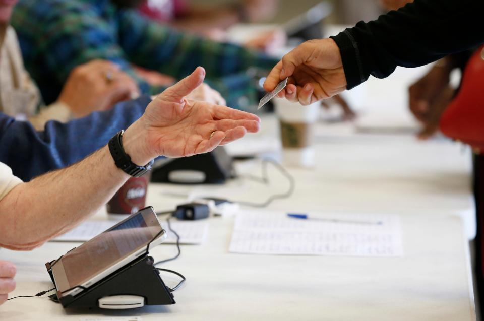 A Madison County poll worker reaches for voter identification prior to allowing a person to vote during the primary election at the precinct in the Highland Colony Baptist Church in Madison on Tuesday, March 8, 2016.