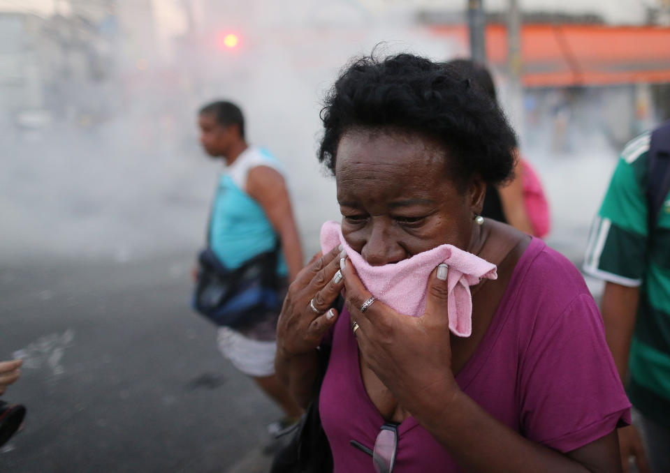 A woman covers her face to protect herself against tear gas used by police during a protest against a bus fare increase in Rio de Janeiro, Brazil, Thursday, Feb. 6, 2014. Last year, millions of people took to the streets across Brazil complaining of higher bus fares, poor public services and corruption while the country spends billions on the World Cup, which is scheduled to start in June. (AP Photo/Leo Correa)