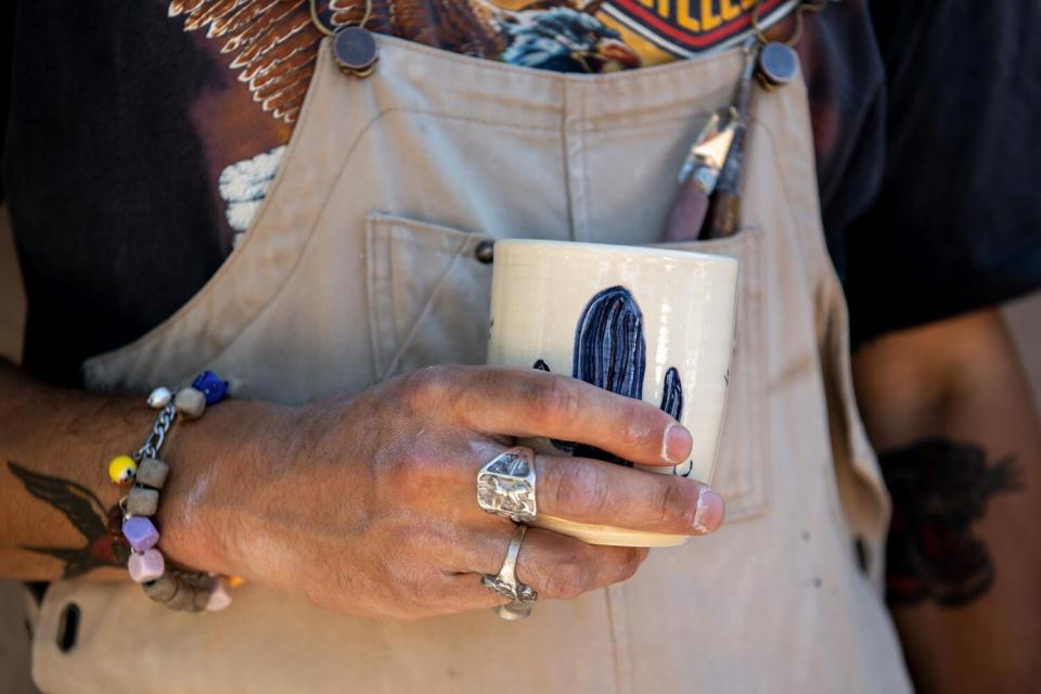 Daniel Dooreck holds a piece of pottery with a blue carved cactus