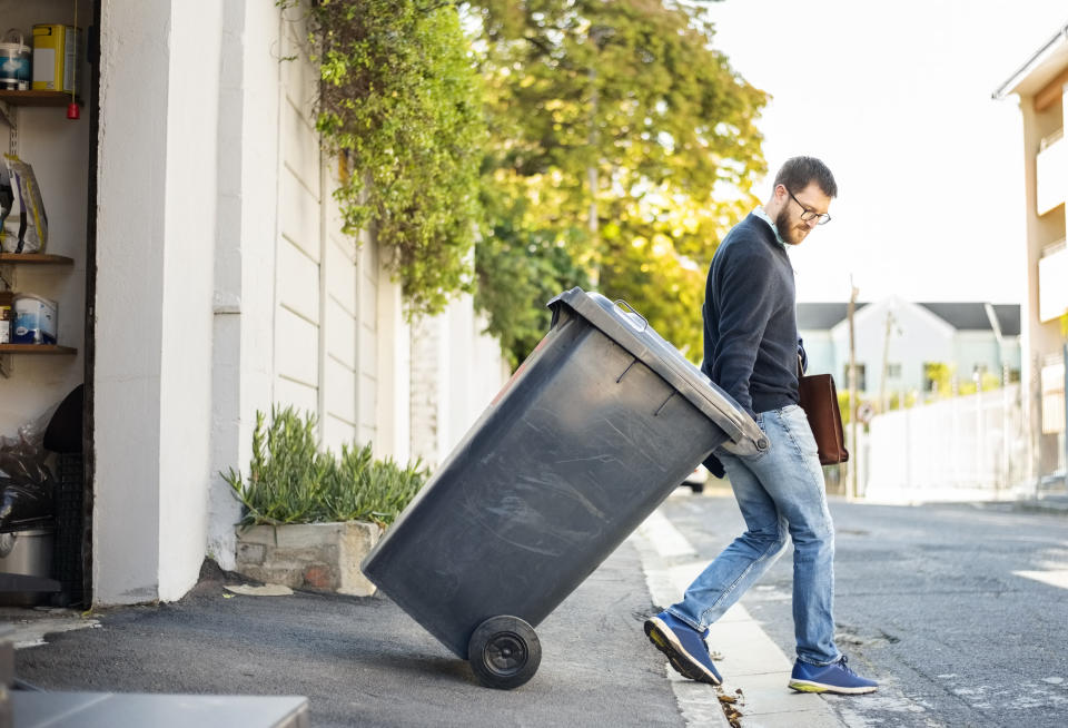 Man bringing a trash can out of his garage