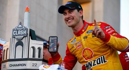 Joey Logano celebrates with the trophy and his family on the phone after winning the Busch Light Clash in Los Angeles