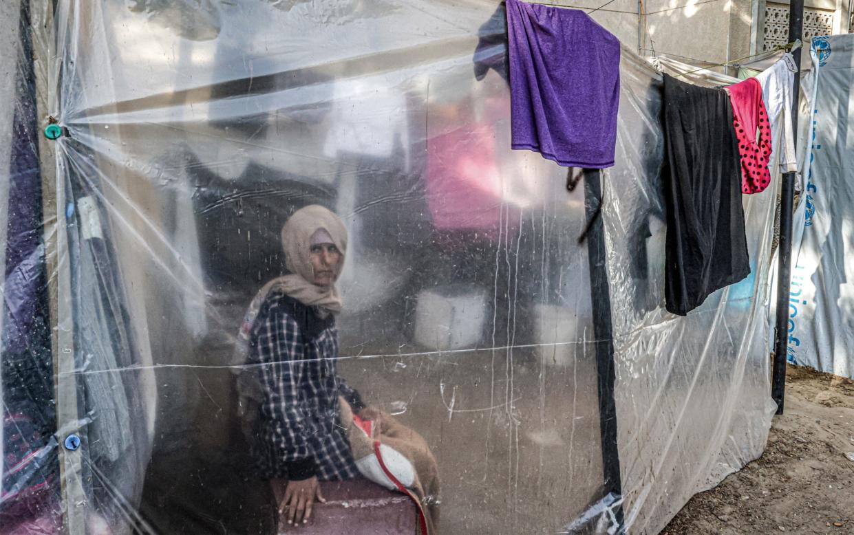 A woman looks on from behind a plastic screen as she sits by clothes hanging on a laundry line at a camp housing displaced Palestinians outside the European Hospital in Khan Yunis in the southern Gaza Strip