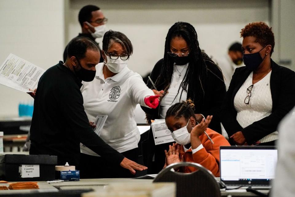 People wearing face mask, some sitting and some standing, seem to be in a discussion.