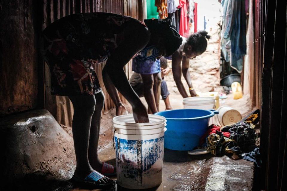 Linet (L), 16, who is about 3 months pregnant, helps to wash clothes.