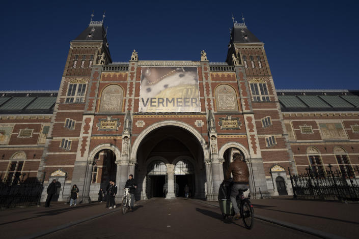 Cyclists pass under the Vermeer exhibit sign at Amsterdam's Rijksmuseum, Monday, Feb. 6, 2023, which unveils its blockbuster exhibition of 28 paintings by 17th-century Dutch master Johannes Vermeer drawn from galleries around the world. (AP Photo/Peter Dejong)