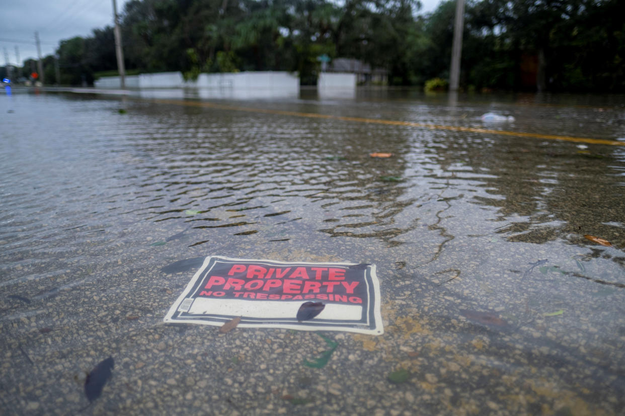 A sign ripped out by the storm saying Private Property, No Trespassing, lies in a flooded street.