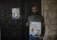 Palestinian Moayyad al-Alami, father of slain Mohammed al-Alami, 12, carry a poster with picture and name of his son and reads "Palestinian National Liberation movement, Fatah, offers her hero martyr child," at the family house, in the West Bank village of Beit Ummar, near Hebron, Wednesday, Aug. 4, 2021. (AP Photo/Nasser Nasser)