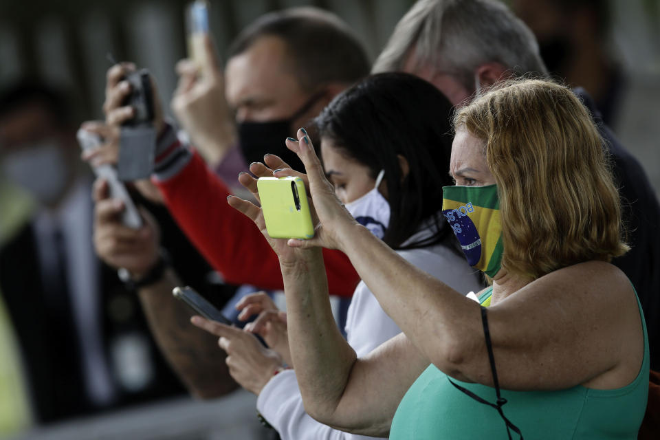 Supporters of Brazil's President Jair Bolsonaro, wearing face masks amid the new coronavirus pandemic, photograph the president's departure from his official residence of Alvorada palace in Brasilia, Brazil, Monday, May 25, 2020. (AP Photo/Eraldo Peres)