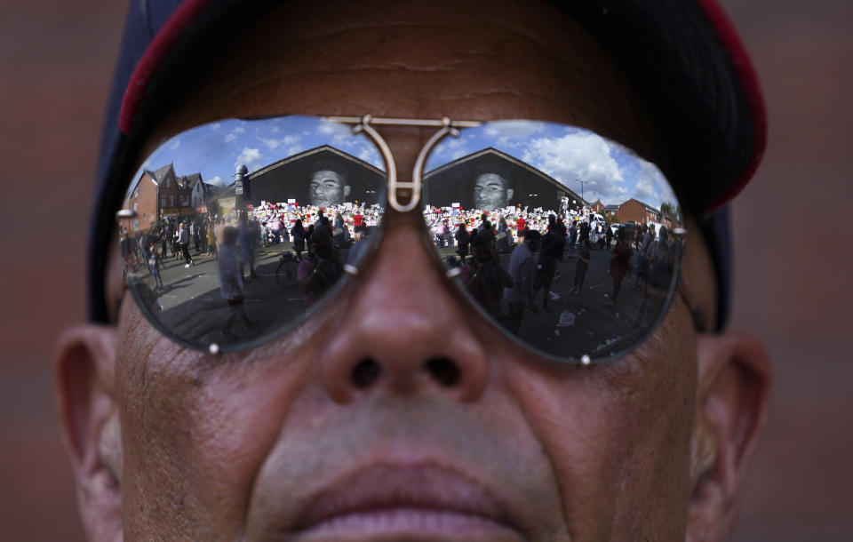 FILE - People are reflected in a man's sunglasses looking at the messages of support left on a mural of Manchester United striker and England player Marcus Rashford, on the wall of the Coffee House Cafe on Copson Street, in Withington, Manchester, England, Tuesday July 13, 2021. The mural was defaced with abusive graffiti in the wake of England losing the Euro 2020 soccer championship final match to Italy. The manifestation of a deeper societal problem, racism is a decades-old issue in soccer — predominantly in Europe but seen all around the world — that has been amplified by the reach of social media and a growing willingness for people to call it out. (AP Photo/Jon Super, File)