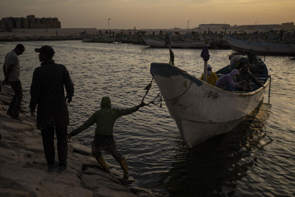 Hombres se preparan para atracar una embarcación tradicional de pesca, conocidas como piraguas, en el puerto en Nuadibú, Mauritania, el 27 de noviembre de 2021. (AP Foto/Felipe Dana)