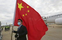 FILE - In this Monday, Feb, 15, 2021 file photo, an official from the Chinese embassy in Zimbabwe holds a Chinese flag next to a plane carrying Sinopharm COVID-19 vaccine from China upon arrival at Robert Mugabe International Airport in Harare. Zimbabwe received its first COVID-19 vaccines with the jet carrying 200,000 Sinopharm doses from China. (AP Photo/Tsvangirayi Mukwazhi)