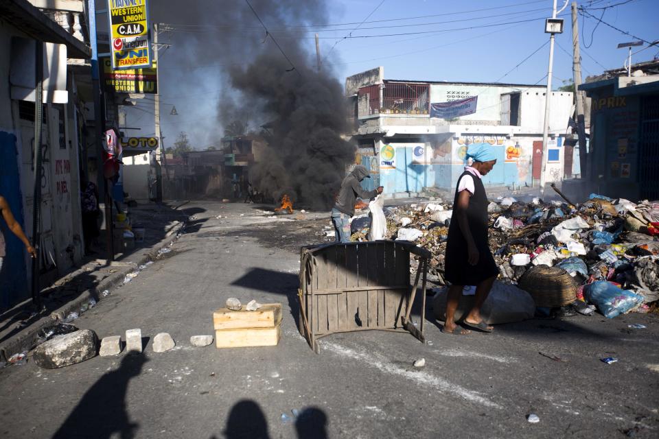 Residents walk near barricades on the third day of a strike and of countrywide protests over allegations of government corruption, in Port-au-Prince, Haiti, Tuesday, Nov. 20, 2018. Demonstrators are calling for the president to resign for not investigating allegations of corruption in the previous government over a Venezuelan subsidized energy program, Petrocaribe. (AP Photo/Dieu Nalio Chery)