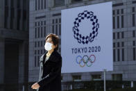 A woman wearing a protective mask to help curb the spread of the coronavirus walks near a banner of the Tokyo 2020 Olympics in Tokyo Tuesday, Jan. 19, 2021. The Tokyo Olympics are to open in six months on July 23. Interestingly, Tokyo organizers have no public program planned to mark the milestone. There is too much uncertainty for that right now. (AP Photo/Eugene Hoshiko)