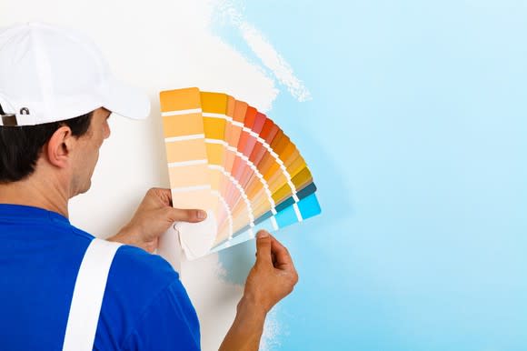 A house painter holds paint samples up to a wall.