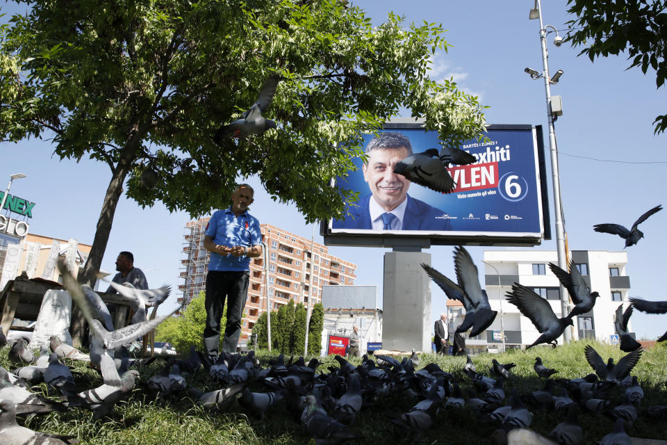 A man feeds pigeons near an electoral poster of Izet Mexhiti from the ethnic Albanian opposition party VLEN, in a street in Skopje, North Macedonia, on Monday, May 6, 2024. Voters go to the polls on Wednesday in North Macedonia to cast ballots for parliamentary election and presidential runoff, for the second time in two weeks. (AP Photo/Boris Grdanoski)