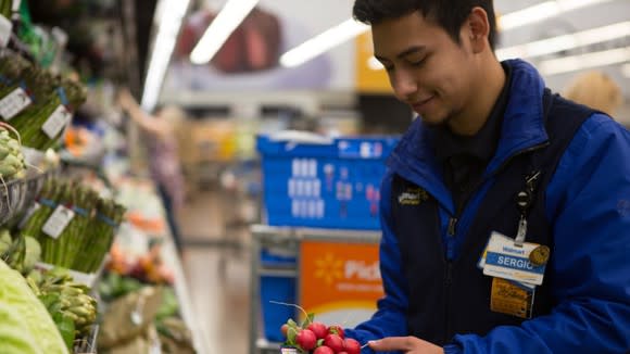 A Walmart employee putting vegetables on display.