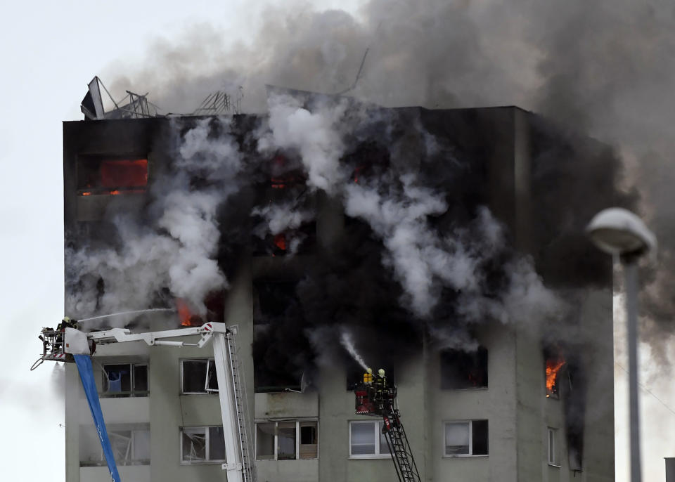 Firefighters on a ladder try to extinguish a fire in a 12-storey apartment block after a gas explosion in Presov, Slovakia, Friday, Dec. 6, 2019. Officials say a gas explosion in an apartment block in Slovakia has killed at least five people and others are trapped on the roof of the building. Firefighters say the explosion occurred in a 12-story building in the city of Presov shortly after noon on Friday. (Frantisek Ivan/TASR via AP)