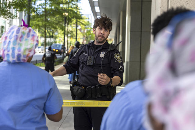 A law enforcement officer speaks to workers in front of Northside Hospital Midtown medical office building, Wednesday, May 3, 2023, in Atlanta, where five people were shot. (Arvin Temkar/Atlanta Journal-Constitution via AP)