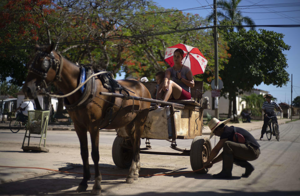 A man pumps the wheel of his horse-drawn carriage as his family waits in San Nicolas, Cuba, Friday, May 19, 2023. (AP Photo / Ramon Espinosa)