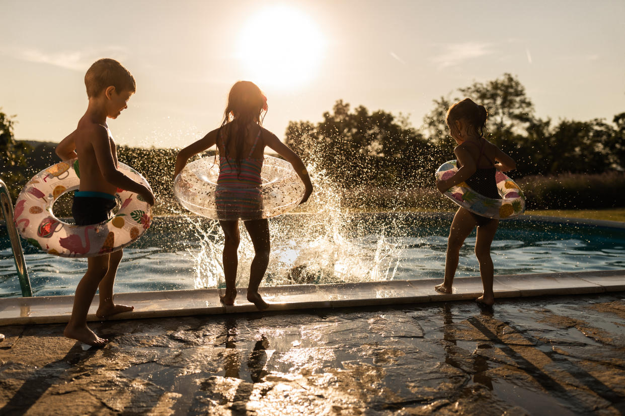 Three small children play next to a swimming pool.