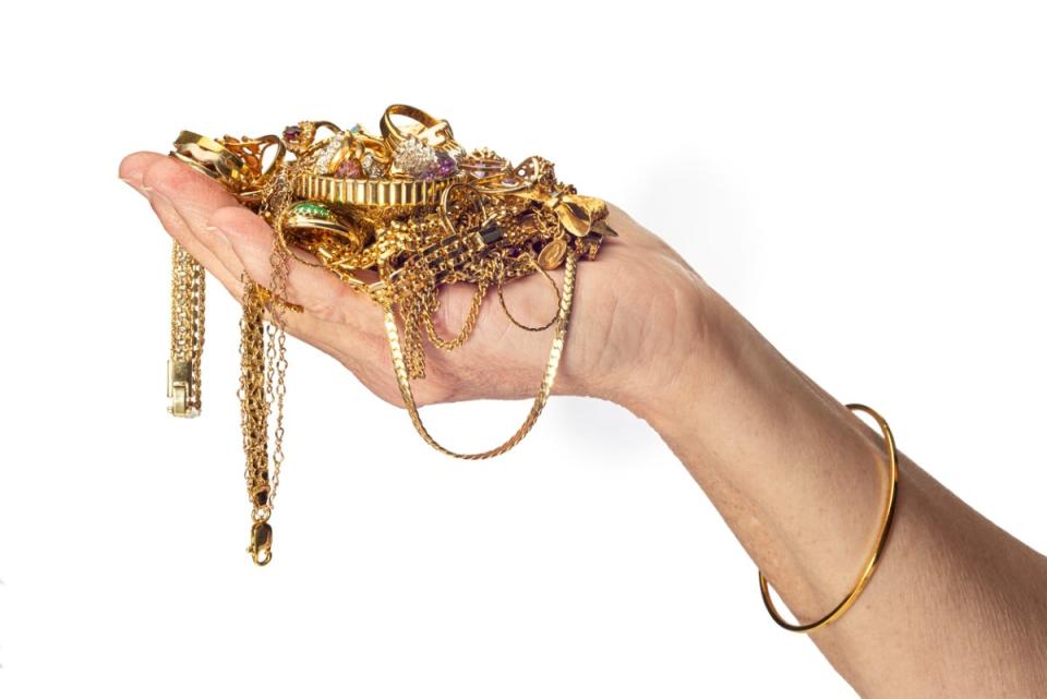 Woman holding lots of tangled gold necklaces, bracelets, and rings in the palm of her hand.