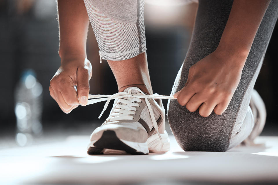 Woman leaning on one knee to tie up her running shoe laces.