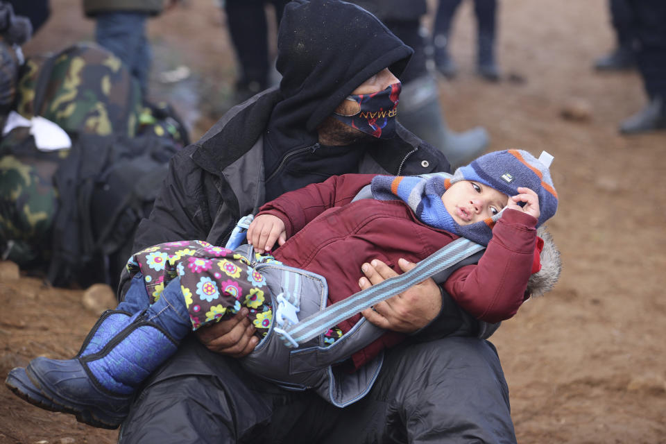 Migrants from the Middle East and elsewhere, one holding his child, gather at the Belarus-Poland border near Grodno, Belarus, Monday, Nov. 8, 2021. Poland increased security at its border with Belarus, on the European Union's eastern border, after a large group of migrants in Belarus appeared to be congregating at a crossing point, officials said Monday. The development appeared to signal an escalation of a crisis that has being going on for months in which the autocratic regime of Belarus has encouraged migrants from the Middle East and elsewhere to illegally enter the European Union, at first through Lithuania and Latvia and now primarily through Poland. (Leonid Shcheglov/BelTA via AP)